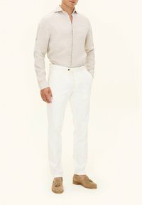 Camicia di lino leggera color beige, pantaloni bianchi su misura e mocassini in suede beige con nappine. Linee semplici e pulite e design aderente.