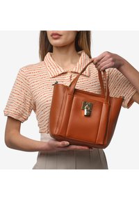 Sac en cuir marron avec poignées doubles, une forme structurée, un fermoir à verrou et des coutures discrètes. Texture lisse avec une finition polie.