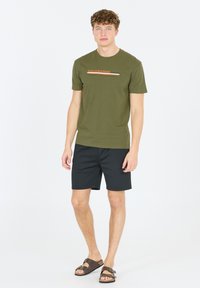 Oliven grøn T-shirt med teksten "YELLOWSTONE", parret med sorte shorts og brune sandaler. Enkel, tætsiddende design med korte ærmer.