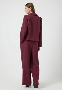 Traje ajustado burdeos con una chaqueta corta y pantalones de pierna ancha, confeccionado en una tela suave. Cuenta con un collar con muescas y mangas rectas.