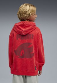 Czerwona bluza z kapturem z dużym czarnym logo graficznym i napisem z tyłu, wykonana z miękkiego materiału o lekko postarzanym wykończeniu.