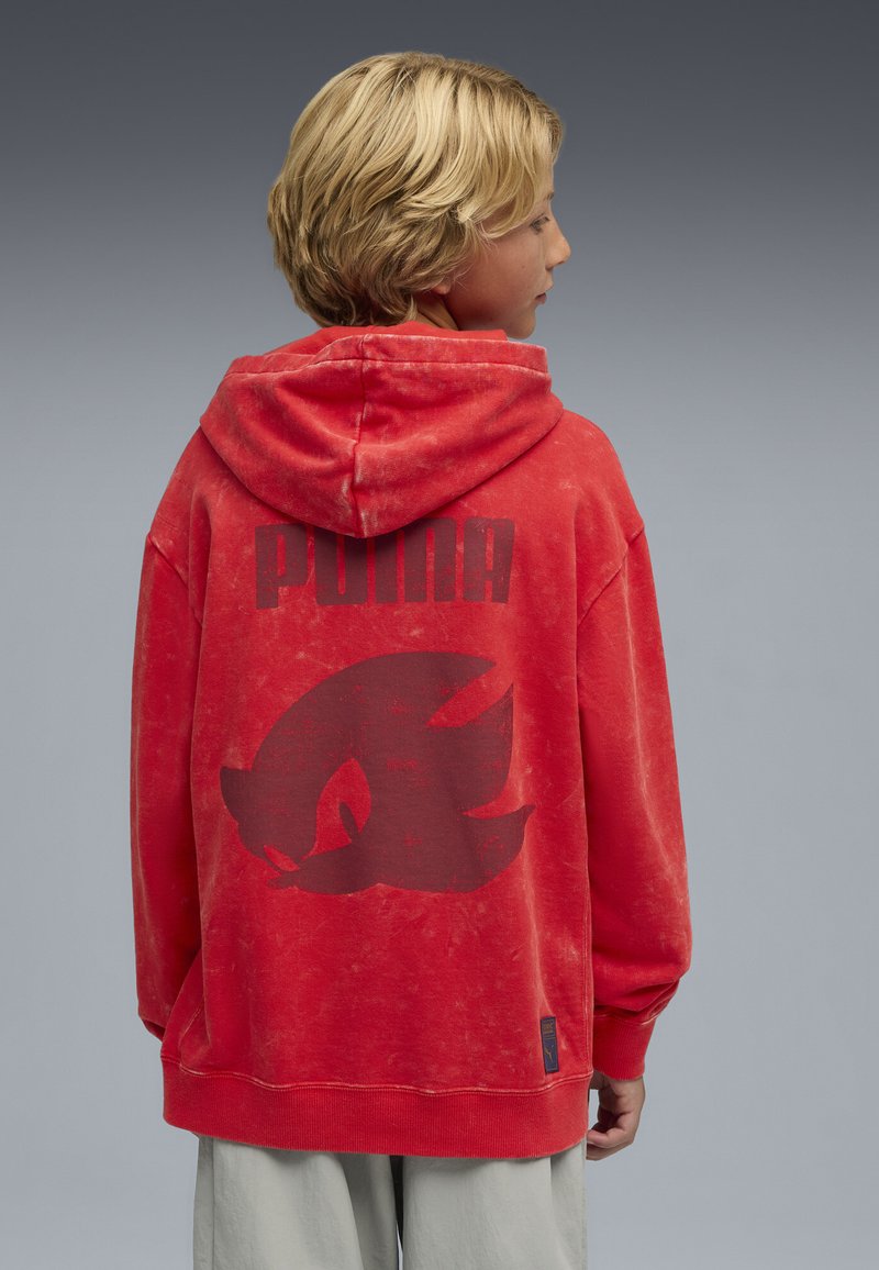 Czerwona bluza z kapturem z dużym czarnym logo graficznym i napisem z tyłu, wykonana z miękkiego materiału o lekko postarzanym wykończeniu.