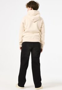 Felpa beige con cappuccio e vestibilità rilassata, abbinata a jeans neri con un classico design a cinque tasche e cuciture marroni.