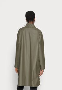 Cappotto impermeabile verde, di lunghezza media, con colletto alto, maniche lunghe e aperture laterali per facilitare i movimenti. Texture liscia, design semplice.