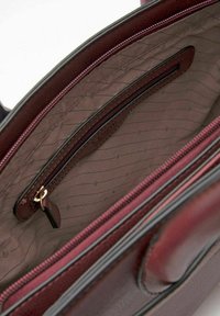 Intérieur de sac à main en cuir couleur bordeaux profond avec une doublure texturée, comprenant une poche zippée et des rayures horizontales. Accents de quincaillerie dorée.