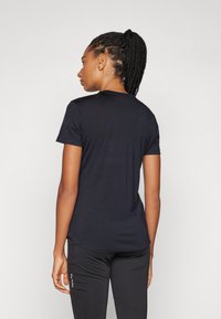Camiseta negra de manga corta con cuello redondo, textura suave y un ligero curvado en el dobladillo, combinada con pantalones deportivos negros.