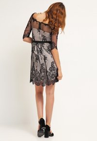 Abito in pizzo nero con maniche corte e trasparenti, corsetto aderente e gonna svasata. Presenta intricati motivi floreali e una cintura nera.