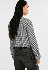 Schwarz-weißer Gingham-Karo-Hemd mit langen Ärmeln und geknöpften Manschetten, kombiniert mit dunkelgrauen, hoch taillierten Jeans mit Gesäßtaschen.