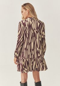 Robe à manches longues, longueur genou en violet foncé avec un motif abstrait crème, dotée d'un ourlet volanté et de poignets élastiques. Texture de tissu lisse.