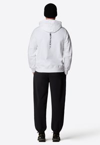 Vit hoodie med dragsnodd, med en svart logotyp på baksidan. Kombineras med svarta byxor och mörka skor för en avslappnad look.