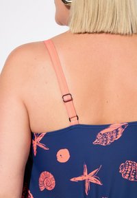 Marine tanktop met koraalkleurige bandjes, versierd met roze schelp- en zee sterpatteren. Verstelbare band met een zwart schuifdetail. Rijke textuur.