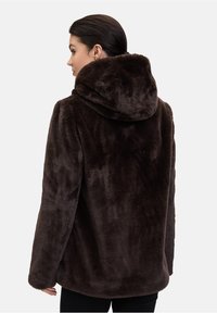 Cappotto in finta pelliccia marrone con cappuccio, caratterizzato da una texture morbida e una vestibilità ampia, che mette in mostra un design semplice privo di accessori o decorazioni.