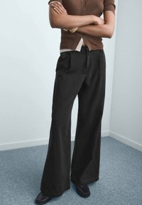 Sorte breddebenede jeans lavet af denim, med forlommer, høj talje og en ren finish. Bæres med en tætsiddende brun top.
