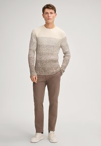 Strickpullover mit einem Farbverlauf von Creme zu Hellbraun, gerippte Textur, runder Ausschnitt. Kombiniert mit braunen Hosen und weißen Sneakers.