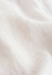 Helles beige Leinengewebe mit einer weichen, strukturierten Oberfläche, die ein dezentes Webmuster und sanfte Falten zeigt.