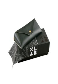Custodia per occhiali in pelle nera con chiusura a scatto dorata, posizionata su una scatola nera con un motivo geometrico bianco e un panno per la pulizia.