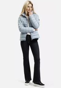 Jasnoniebieska, pikowana kurtka z wysokim kołnierzem, z zapięciem na zamek i czarnymi detalami w postaci naszywki; zestawiona z czarnymi spodniami dzwonami i czarnymi sneakersami.