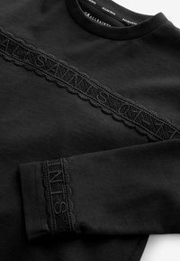 Must mustra lõngast sweatshirt, millel on keerukad pitskorrused rinna ja varrukate ääres, kaunistatud sakilise serva detailiga.