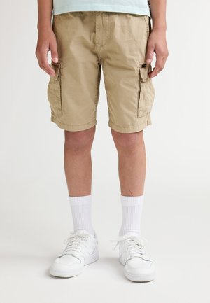 Beige cargoshorts met zijzakken, gemaakt van katoen, kniehoog. Gecombineerd met witte sportsokken en witte sneakers.