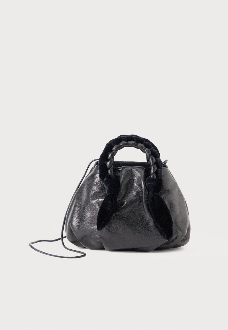 Schwarze Lederhandtasche mit geflochtenem Samtgriff und dünnem Schulterband, vor einem schlichten hellen Hintergrund.