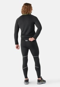 Sort atletisk top med en grøn krave, parret med sorte leggings med reflekterende accenter, og grå-sorte atletiske sko.