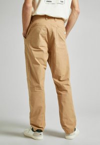 Pantalones de algodón beige con un corte relajado, que cuentan con dos bolsillos traseros y detalles de costura sutiles. Llevados con zapatillas blancas.