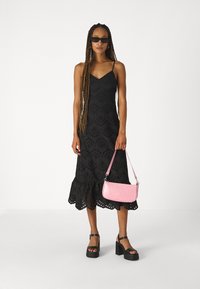Vestido preto com ilhós e bainha rodada, complementar por uma mala de textura rosa e sandálias plataforma pretas. Design com alças e corpete ajustado.