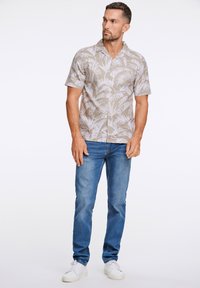 Korte mouwen overhemd met knopen in lichtbeige met een wit palmenbladpatroon. Gecombineerd met blauwe jeans en witte sneakers. Eenvoudig, casual ontwerp.