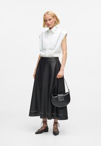 Woman wearing a white studded sleeveless shirt, black studded A-line skirt, lace-up flats, and holding a black studded handbag.