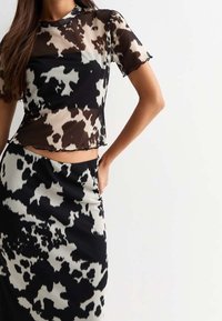 Top con stampa mucche nera e crema con maniche corte, abbinato a una gonna a vita alta coordinata. Materiale trasparente, design aderente.
