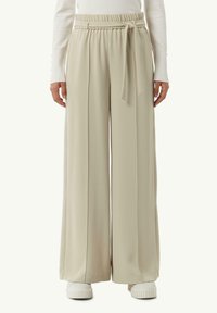 Beige wijde broek met een hoge elastische tailleband en een gevlochten riemdetail. Soepele, vloeiende stof met plooien aan de voorkant en een ontspannen pasvorm.