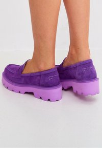 Scarpe in suede viola con suola spessa e texture di un viola chiaro, design slip-on. I dettagli di cucitura sono visibili sulla parte superiore.