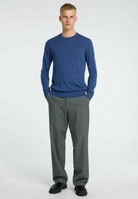 Blå stickad tröja i kombination med grå byxor. Tröjan har en rund halsringning och långa ärmar; byxorna har en rak passform och är veckade.