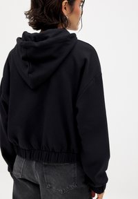 Black cropped hoodie with a soft, textured finish, featuring a drawstring hood and elastic waistband. No visible logos or patterns.