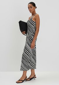 Schwarz-weißer gestreifter Midikleid mit einem Träger, kombiniert mit einer schwarzen strukturierten Tasche und schwarzen High-Heelsandalen. Glattes Material, lässige Passform.