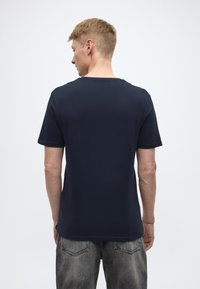 T-shirt blu navy a maniche corte, collo rotondo, realizzata in cotone morbido. Texture liscia, vestibilità leggermente ampia, con un design semplice.