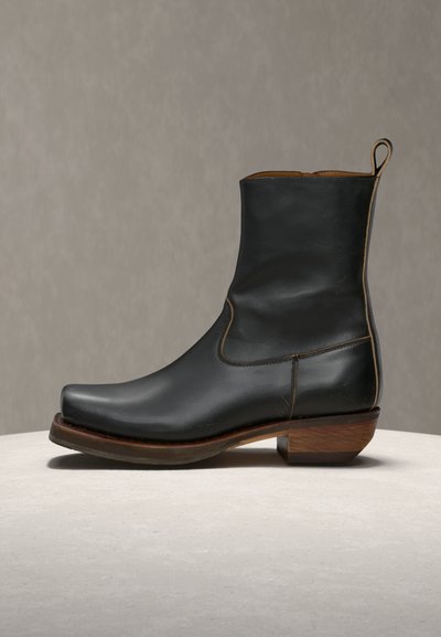 Μαύρο δερμάτινο μποτάκι μέχρι τον αστράγαλο με τετράγωνη μύτη, ξύλινο τακούνι και ταινία έλξης, σε ουδέτερη επιφάνεια και φόντο.