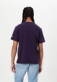 Lilla bomulds t-shirt med korte ærmer og rund hals. Har et enkelt design uden synlige mønstre eller grafik på ryggen.