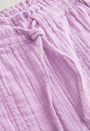 Pantaloni moi de in, de culoare liliac deschis, cu talie elastică și șnur legat în față, ce arată textura detaliată a țesăturii și cusăturile.