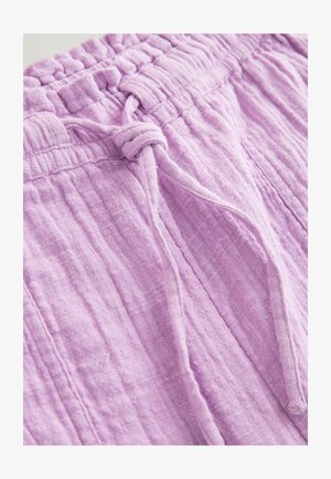 Mäkké svetlofialové ľanové nohavice s elastickým pásom a šnúrkou zviazanou vpredu, zobrazujúce detailnú textúru látky a švy.