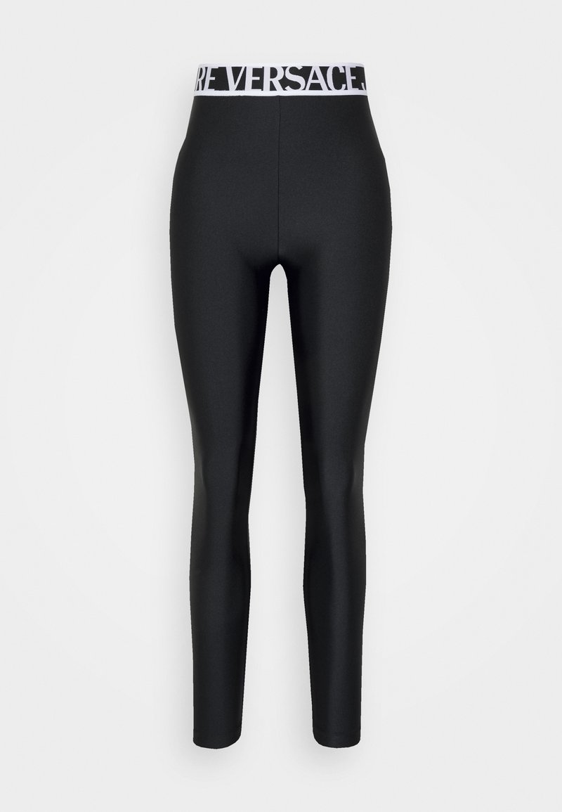 Leggings neri a vita alta con una ampia cintura bianca che presenta un audace logo "VERSACE", mostrati su uno sfondo bianco semplice.