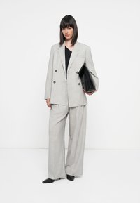 Lys grå oversized dobbeltspent blazer kombinert med brede grå bukser. Modellen holder en svart clutch, iført svart topp og spisse sko.