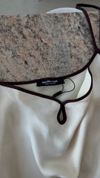 Blouse couleur crème avec un décolleté en V profond, rehaussé de bordeaux foncé, portant une étiquette marquée "Massimo Dutti" et une texture lisse et douce.