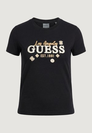 T-shirt nera a maniche corte con la scritta "Los Angeles GUESS EST. 1981" e toppe decorative beige sul davanti.