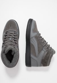 Baskets montantes grises combinant cuir lisse et textures en suède, avec un col rembourré et une semelle en caoutchouc. Détails perforés présents.