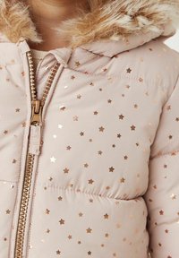 Chaqueta de plumas rosa claro con acentos metálicos en forma de estrellas, capucha con bordes de piel y un zipper dorado. Textura suave y diseño acolchado.