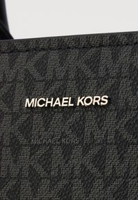 Musta tekstuuripaintumaine kangas, millel on delikaatne muster. Kuldne "MICHAEL KORS" logo on silmapaistvalt olemas, lisades kontrasti kogu disainile.