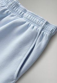 Svetlomodré tepláky s jemnou, flísovou textúrou, vybavené elastickým pásom a bočnými vreckami.