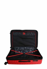 Valigia rigida rossa con una texture esagonale, interno nero, dettagli rossi, cinghie sicure e una patacca con logo all'interno. Aperta per essere riempita.