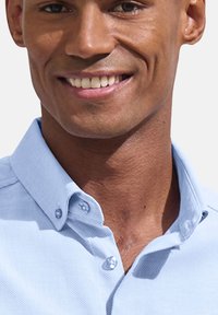 Svetlomodrá košeľa na gombíky s textúrovanou tkaninou, úzkym golierom a viditeľným šitím. Hladký, priliehavý dizajn okolo výstrihu.